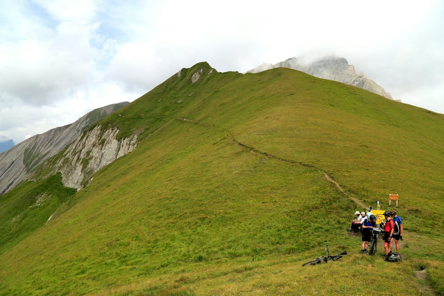 Ciclisti che riposano su un pendio erboso di montagna vicino a una panchina.