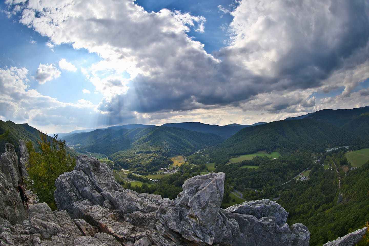 Un escursionista scala formazioni rocciose che dominano un'ampia valle montana verde.