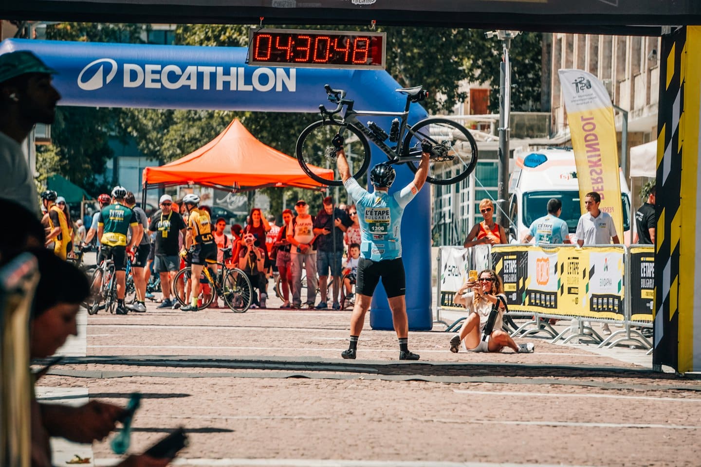 Un ciclista alza trionfante la sua bici sotto un arco gonfiabile.